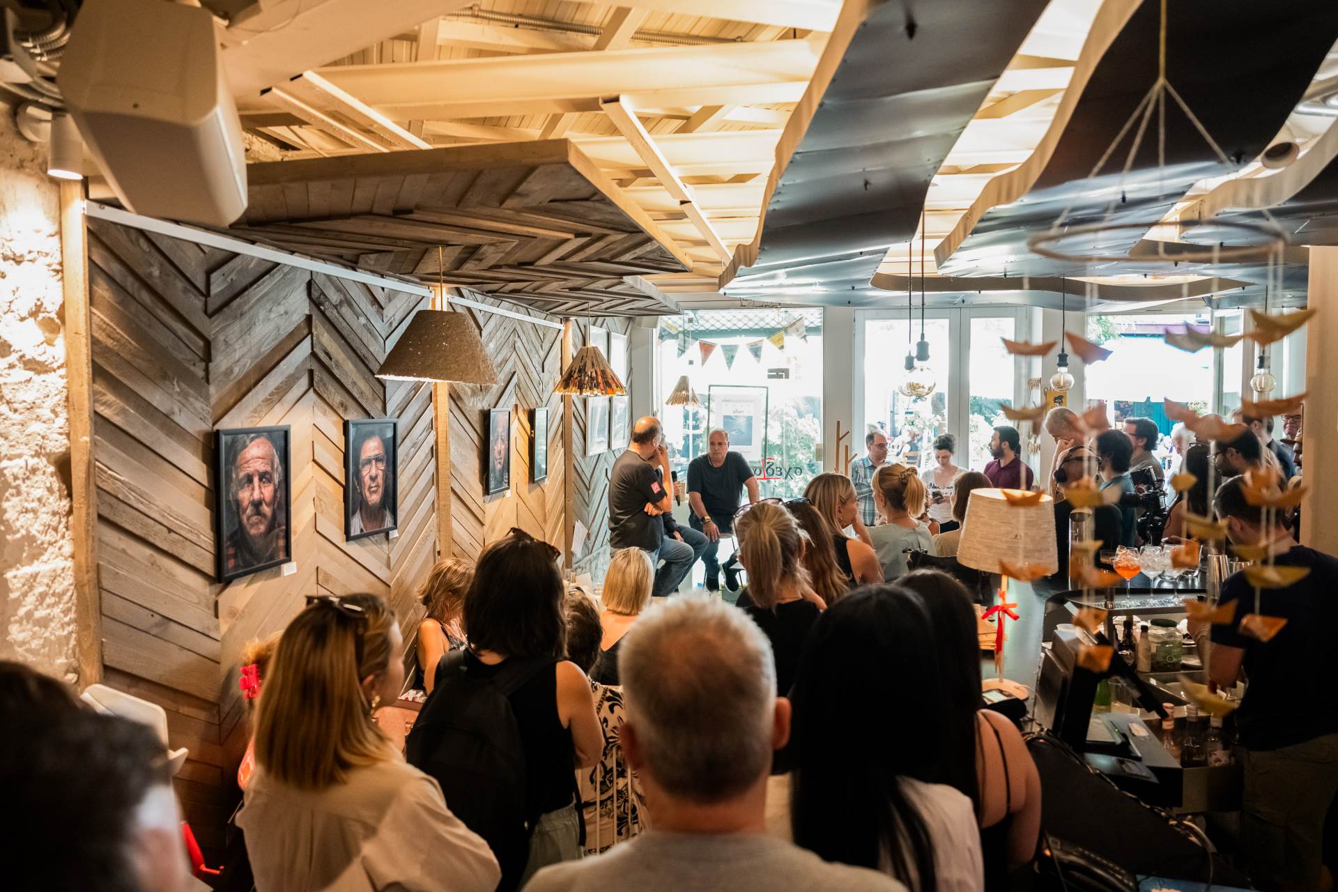 Μια  ομάδα ανθρώπων βρίσκονται σε ένα μπαρ/εστιατόριο, παρακολουθώντας μια συζήτηση.