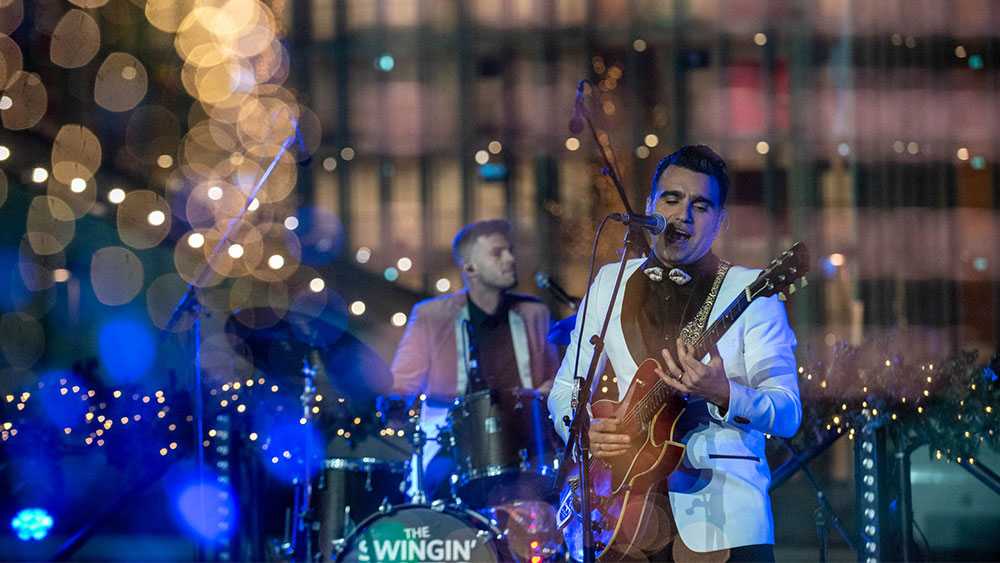 Ένας άνδρας τραγουδάει και παίζει κιθάρα, ενώ ένας άλλος άνδρας παίζει ντραμς από πίσω