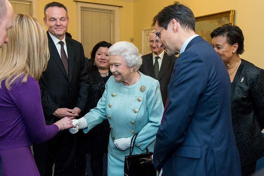 Η βασίλισσα Ελισάβετ σφίγγει το χέρι μιας γυναίκας στη μέση μιας ομάδας ανθρώπων