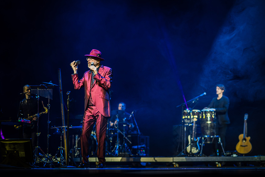 Ένας τραγουδιστής τραγουδάει στη σκηνή, συνοδευόμενος από μια μπάντα