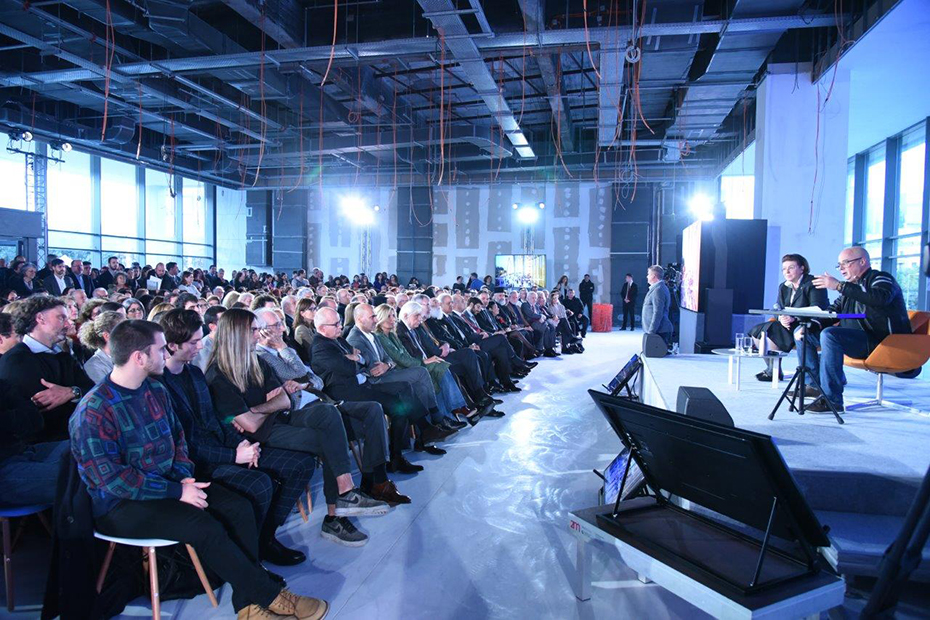 Φωτογραφία που δείχνει το πλήθος να παρακολουθεί τους δύο ομιλητές που κάθονται στη σκηνή 