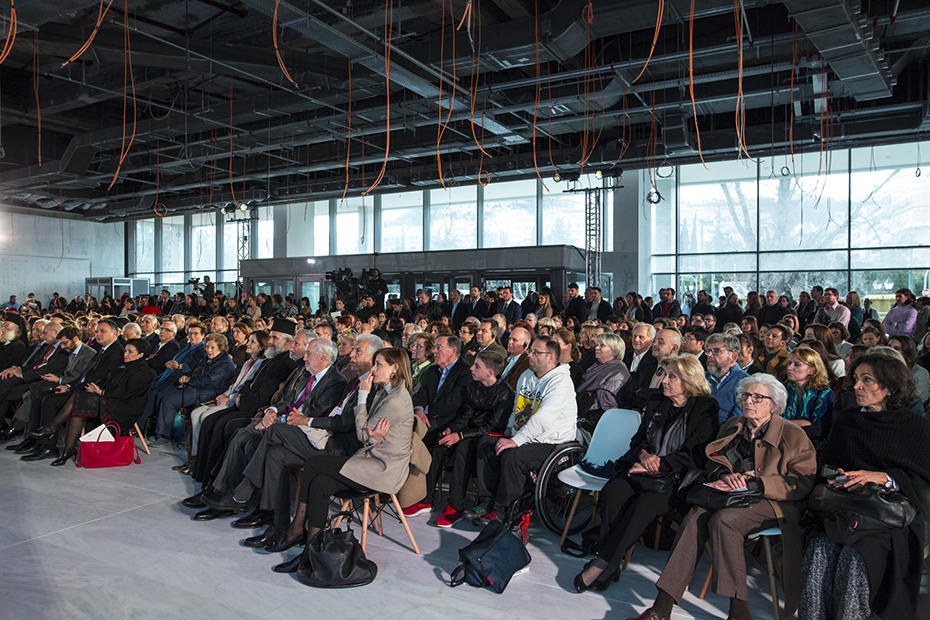 Πλήθος ανθρώπων κάθεται σε καρέκλες και κοιτάει τη σκηνή