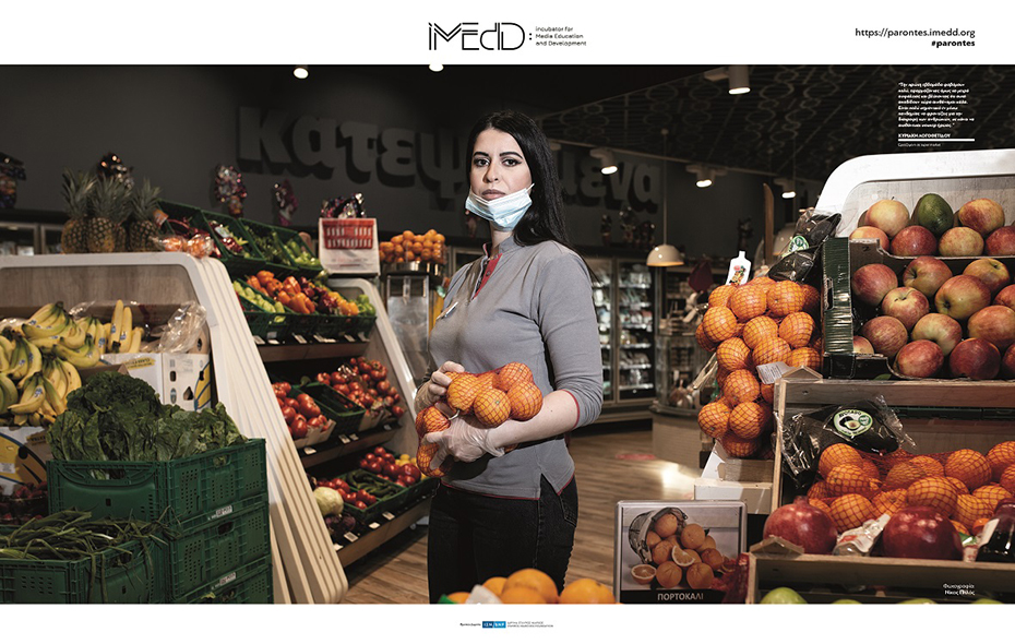 Φωτογραφία που δείχνει μια γυναίκα που δουλεύει στο τμήμα μαναβικής ενός σουπερμαρκετ να κρατάει στην αγκαλιά της πορτοκάλια 