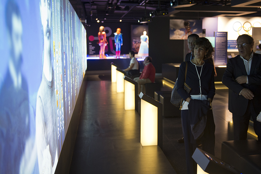 Κόσμος παρακολουθεί τα εκθέματα τα οποία βρίσκονται στον τοίχο μέσω οθονών