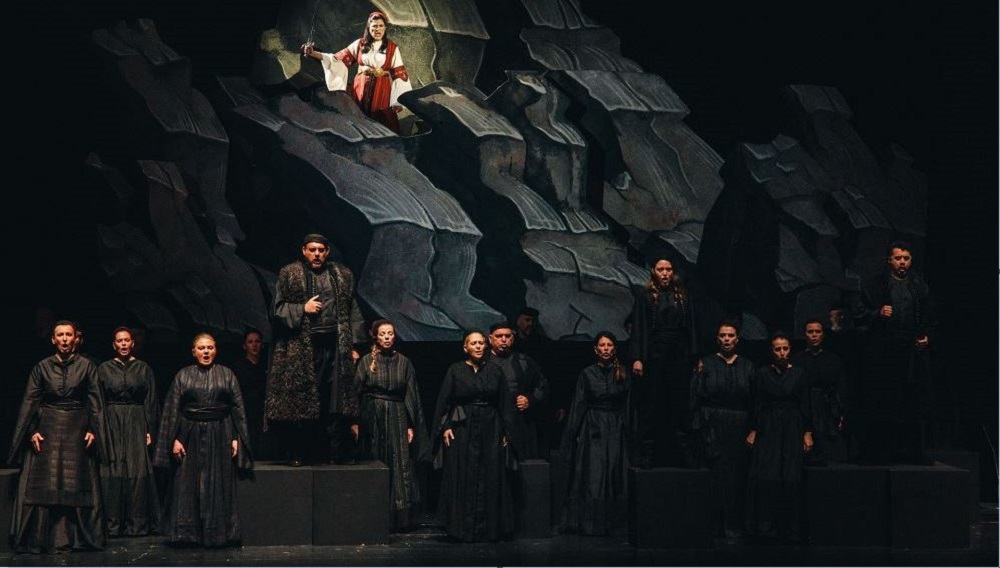 Μια σκηνή στην οποία πολλοί ηθοποιοί ντυμένοι στα μαύρα κοιτούν το κοινό και τραγουδούν στην Εθνική Λυρική Σκηνής