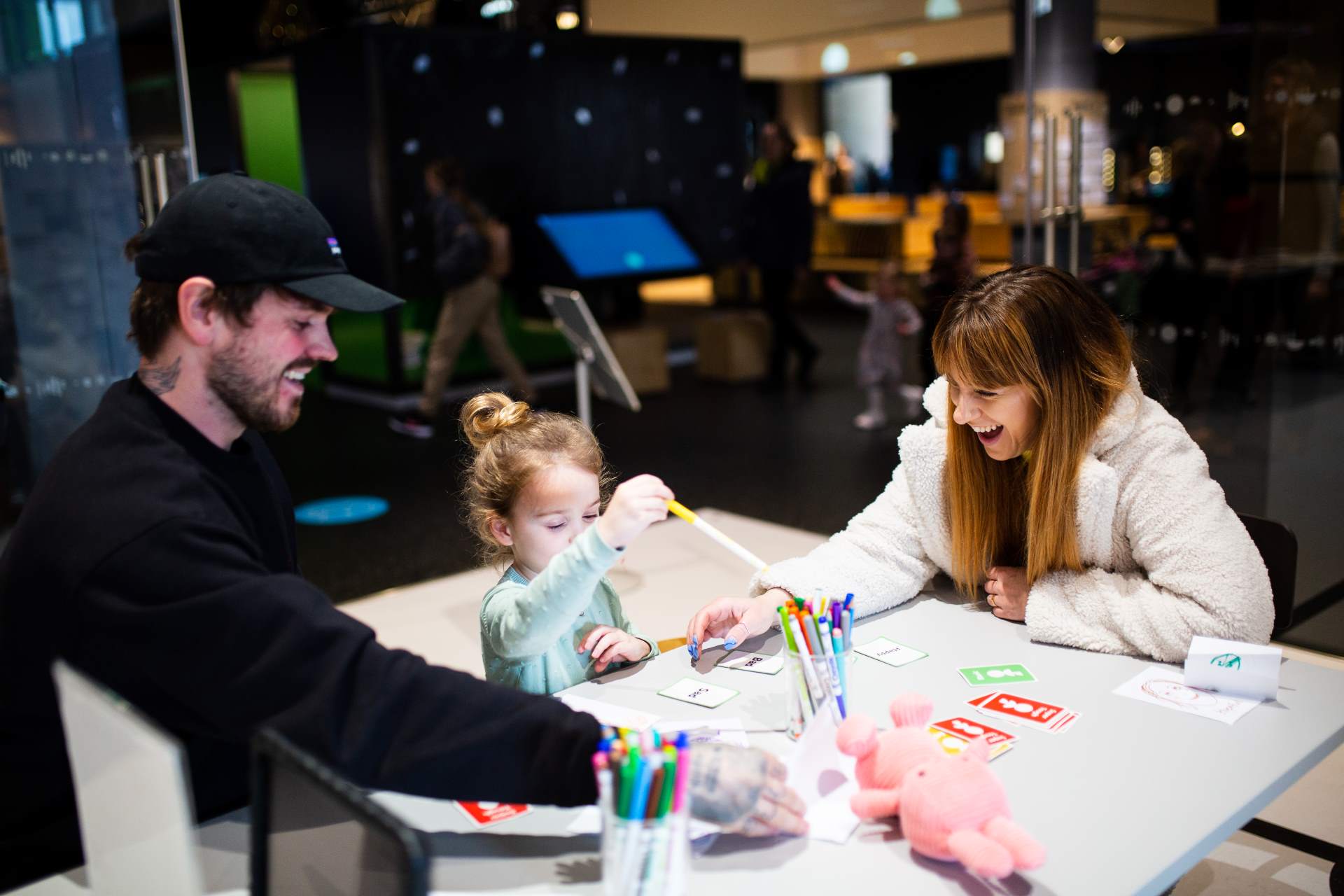 Ένας άνδρας και μια γυναίκα κάθονται σε ένα τραπέζι με ένα παιδί, απολαμβάνοντας να παίζουν ένα επιτραπέζιο παιχνίδι
