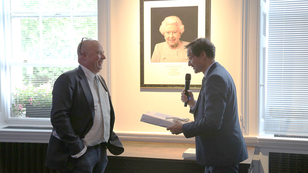 Ο πρόεδρος του Ιδρύματος Σταύρος Νιάρχος Ανδρέας Δρακόπουλος χαμογελάει δίπλα σε έναν άνδρα που κρατά ένα μικρόφωνο και ένα δώρο