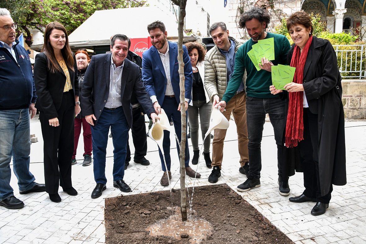 Μια ομάδα ανθρώπων ποτίζει με ποτιστήρια ένα δέντρο που βρίσκεται στον δρόμο 