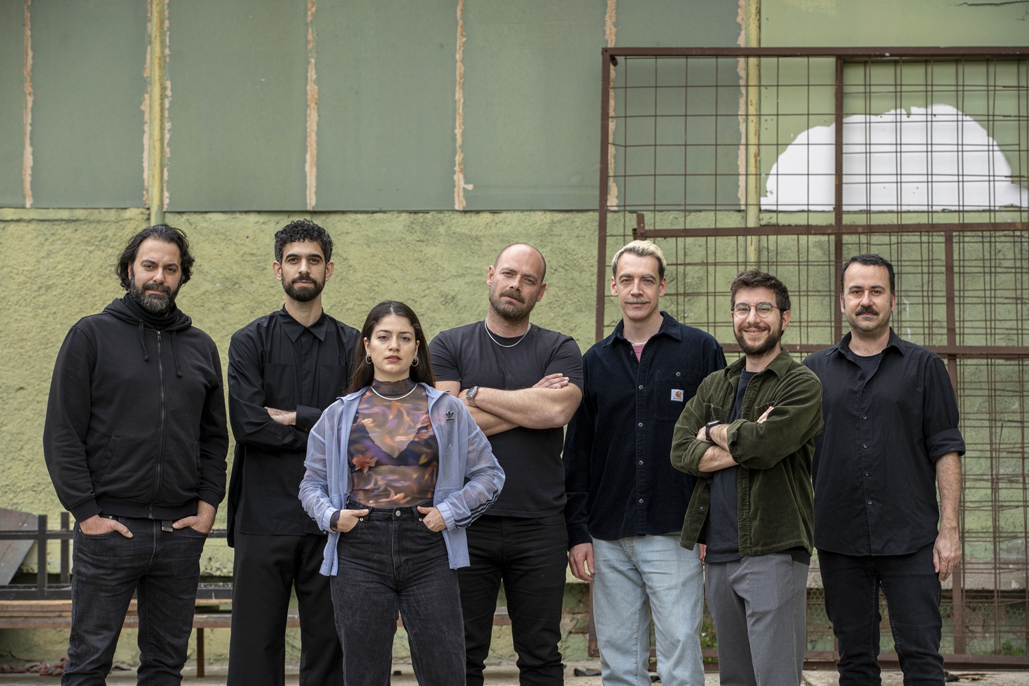 Οι καλλιτέχνες βρίσκονται μπροστά από ένα κτίριο, ποζάροντας με αυτοπεποίθηση για μια φωτογραφία.