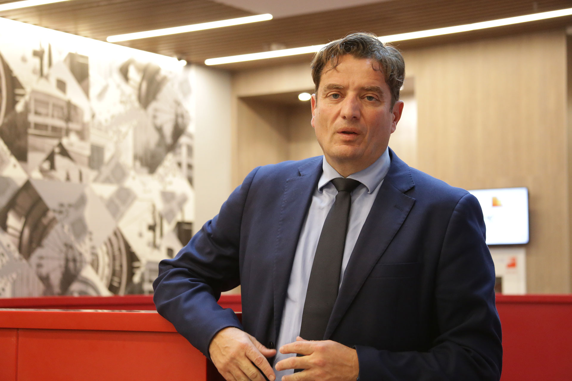 A man in a suit and tie standing in front of a red furniture.