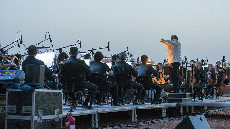 Κοντινή φωτογραφία μιας σκηνής τοποθετημένης στο κέντρο ενός εργοταξίου πάνω στην οποία κάθονται μέλη μιας ορχήστρας με τα όργανά τους