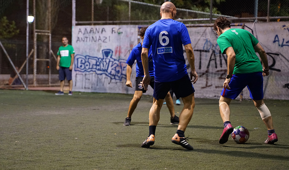 Ένας άνδρας μιας ομάδας προσπαθεί να περάσει δύο άνδρες της αντίπαλης ομάδας σε έναν αγώνα ποδοσφαίρου.