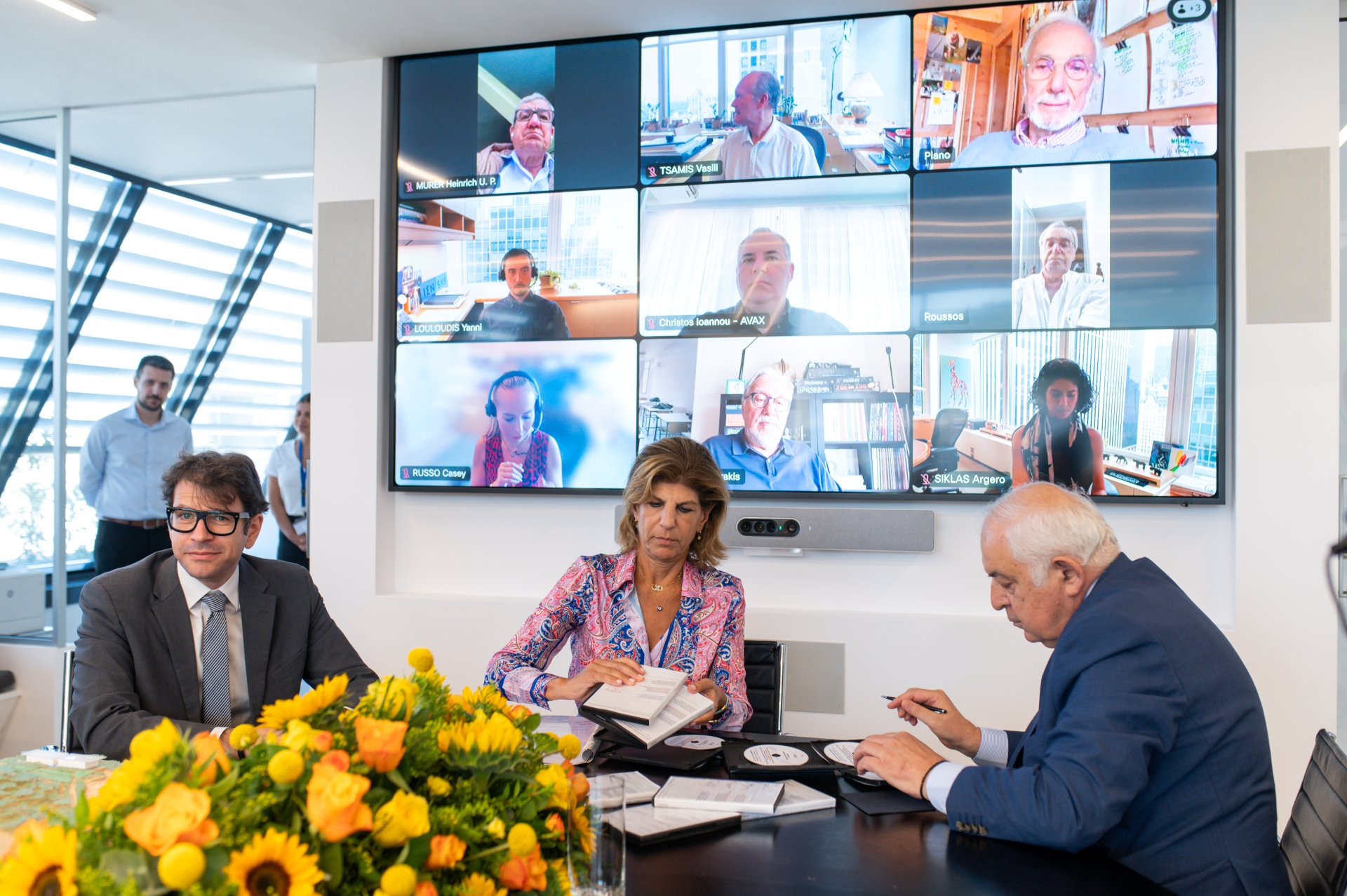 Δύο άντρες και μια γυναίκα μπροστά από ζωντανή σύνδεση με άλλα μέλη του Ιδρύματος Σταύρος Νιάρχος, υπογράφουν για την κατασκευή των τριών νέων νοσκομείων Ίδρυμα Σταύρος Νιάρχος 