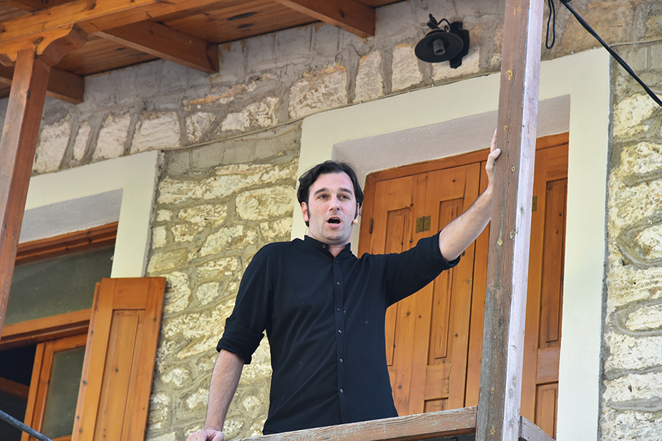 Ένας άντρας στέκεται στο μπαλκόνι ενός πέτρινου παραδοσιακού σπιτιού στο χωριό 