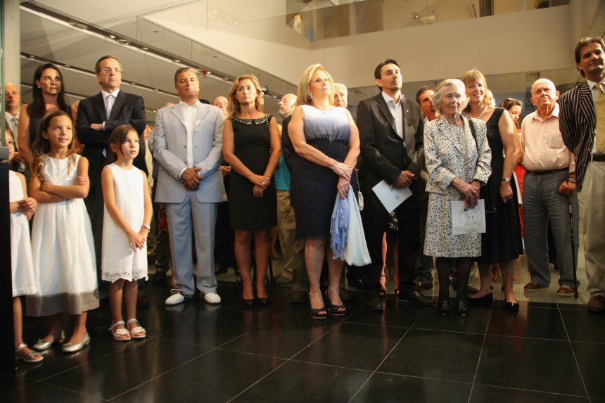 Πλήθος ανθρώπων καθώς και τρία μικρά κορίτσια στέκονται και παρακολουθούν ένα έκθεμα 