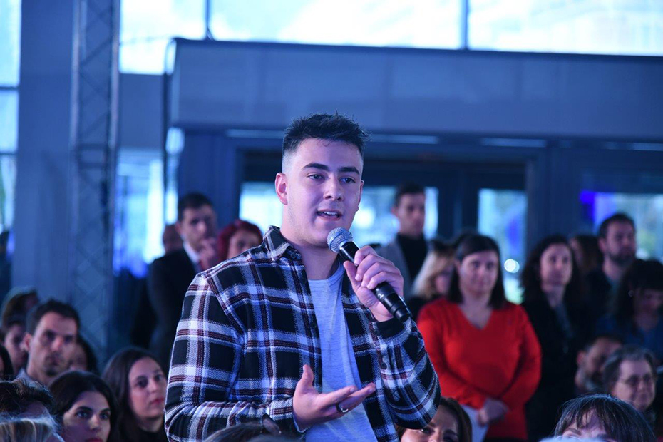 Ένας νέος στέκεται όρθιος ανάμεσα στο κοινό και κάνει μια ερώτηση στο μικρόφωνο 