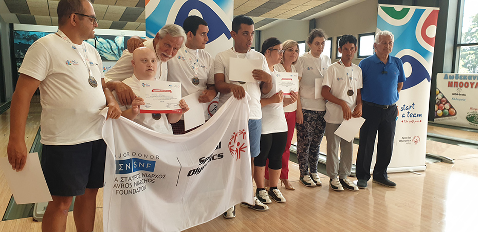 Μια ομάδα ατόμων κρατάνε στα χέρια τους ένα έπαινο και ένα πανό που γράφει Ίδρυμα Σταύρος Νιάρχος Ι Special Olympics 