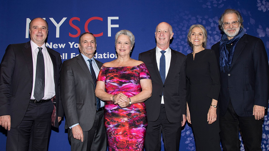 Ο Αντρέας Δρακόπουλος, Πρόεδρος του Ιδρύματος Σταύρος Νιάρχος, βγάζει μια αναμνηστική φωτογραφία μαζί με άλλουτς τρεις άντρες και δύο γυναίκες μπροστά από το banner που γράφει NYSCF