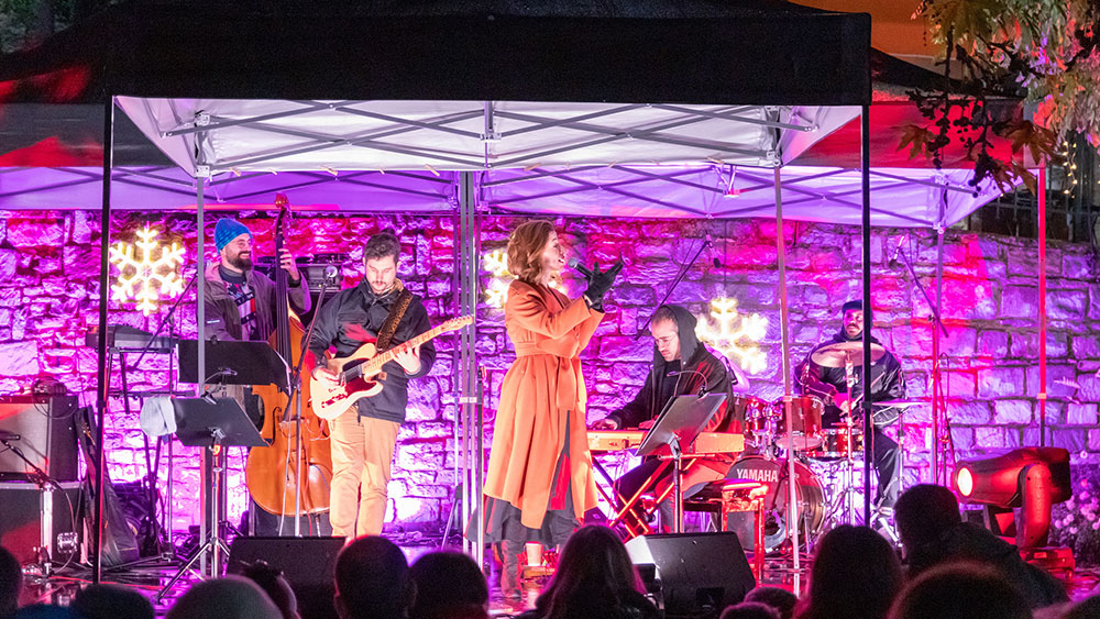 Μια γυναίκα, συνοδευόμενη από μια μπάντα, τραγουδάει σε μια εξωτερική σκηνή μπροστά από κοινό