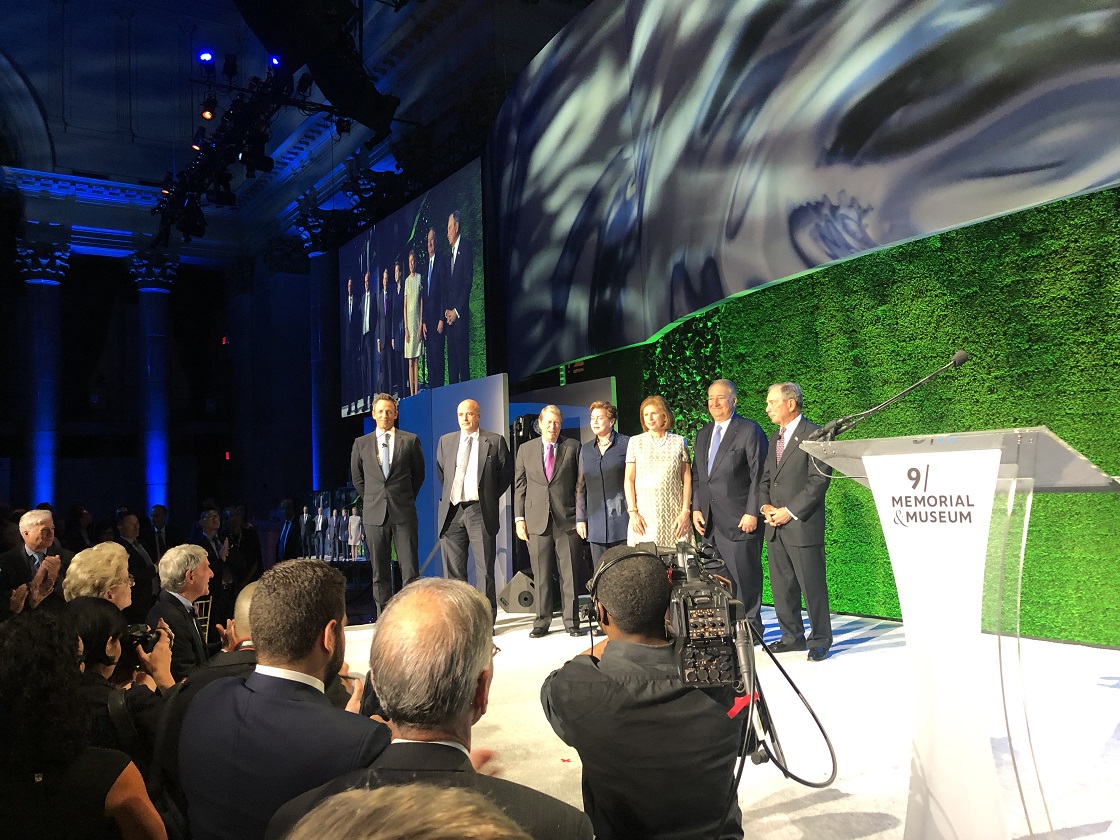 Seven people stand up on stage and a crowd of photographers take pictures of them 