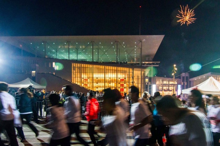 Πλήθος δρομέων τρέχουν τη νύχτα μπροστά από ένα μεγάλο γυάλινο φωτισμένο κτήριο 
