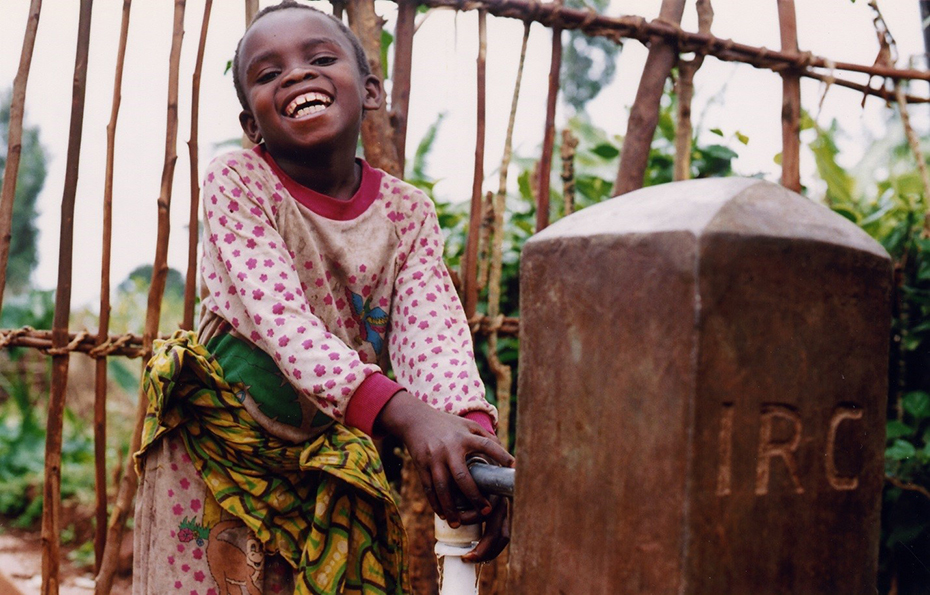 Ένα μικρό κορίτσι χαμογελάει και χρησιμοποιεί μια βρύση νερού