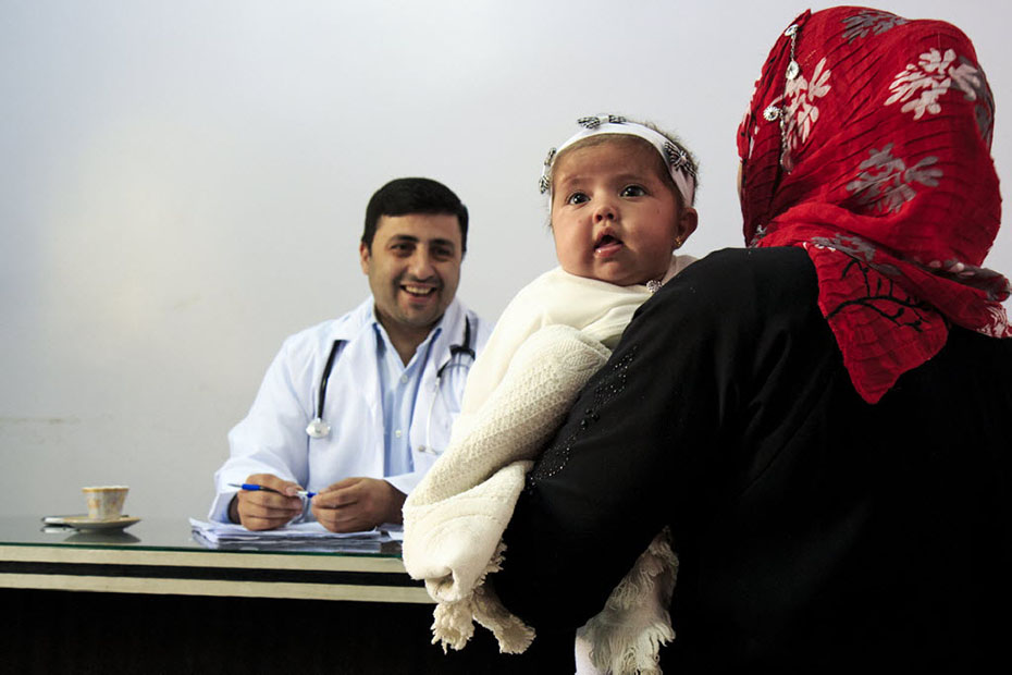 Ένας γιατρός κάθεται στο γραφείο του και χαμογελάει σε μια μητέρα που έχει το μωρό της αγκαλιά