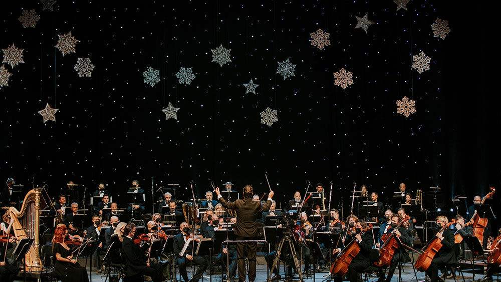 Ένας άνδρας διευθύνει μια ορχήστρα μπροστά από διακοσμήσεις νιφάδων χιονιού