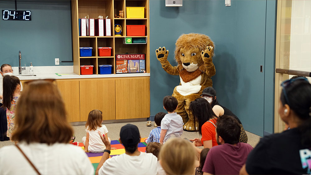Ένα άτομο με στολή λιονταριού διασκεδάζει μικρά παιδιά και γονείς