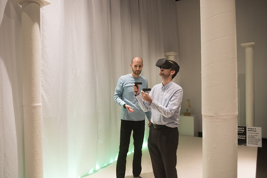 Ένας άντρας βοηθά έναν άλλο άντρα να χρησιμοποιήσει ένα VR headset σε ένα μουσείο