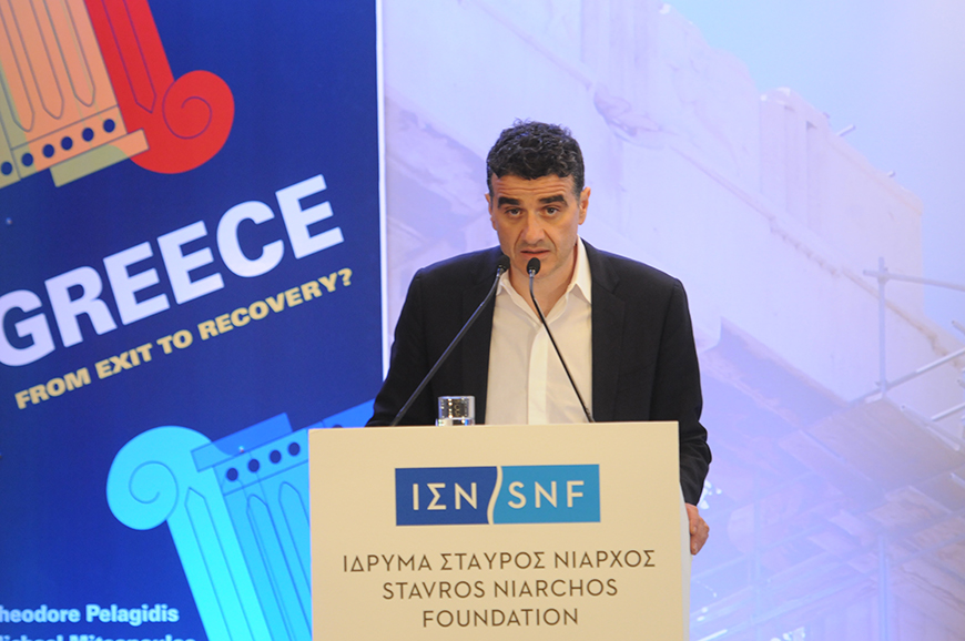 Ένας άντρας βγάζει λόγο στο βήμα του Ιδρύματος Σταύρος Νιάρχος και πίσω του υπάρχει ένα banner το οποίο γράφει GREECE FROM EXIT TO RECOIVERY?
