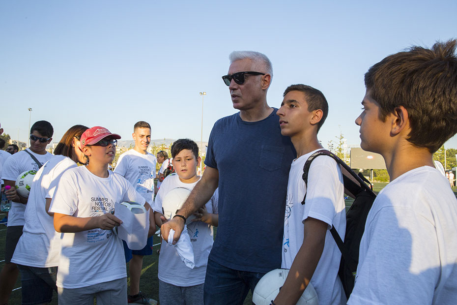 Ένας άντρας περυτριγυρισμένος από νεαρά αγόρια τα οποία κρατρούν μπάλες ποδοσφαίρου στα χέρια τους 