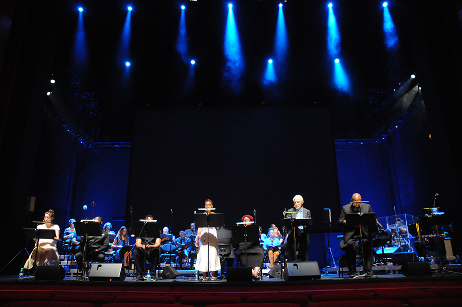 Επτά άτομα τραγουδούν στη σκηνή μπροστά σε μια χορωδία