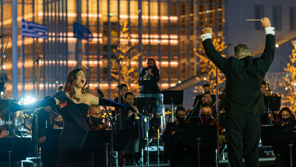 Μια γυναίκα τραγουδά με πάθος δίπλα σε έναν μαέστρο που καθοδηγεί μια ορχήστρα