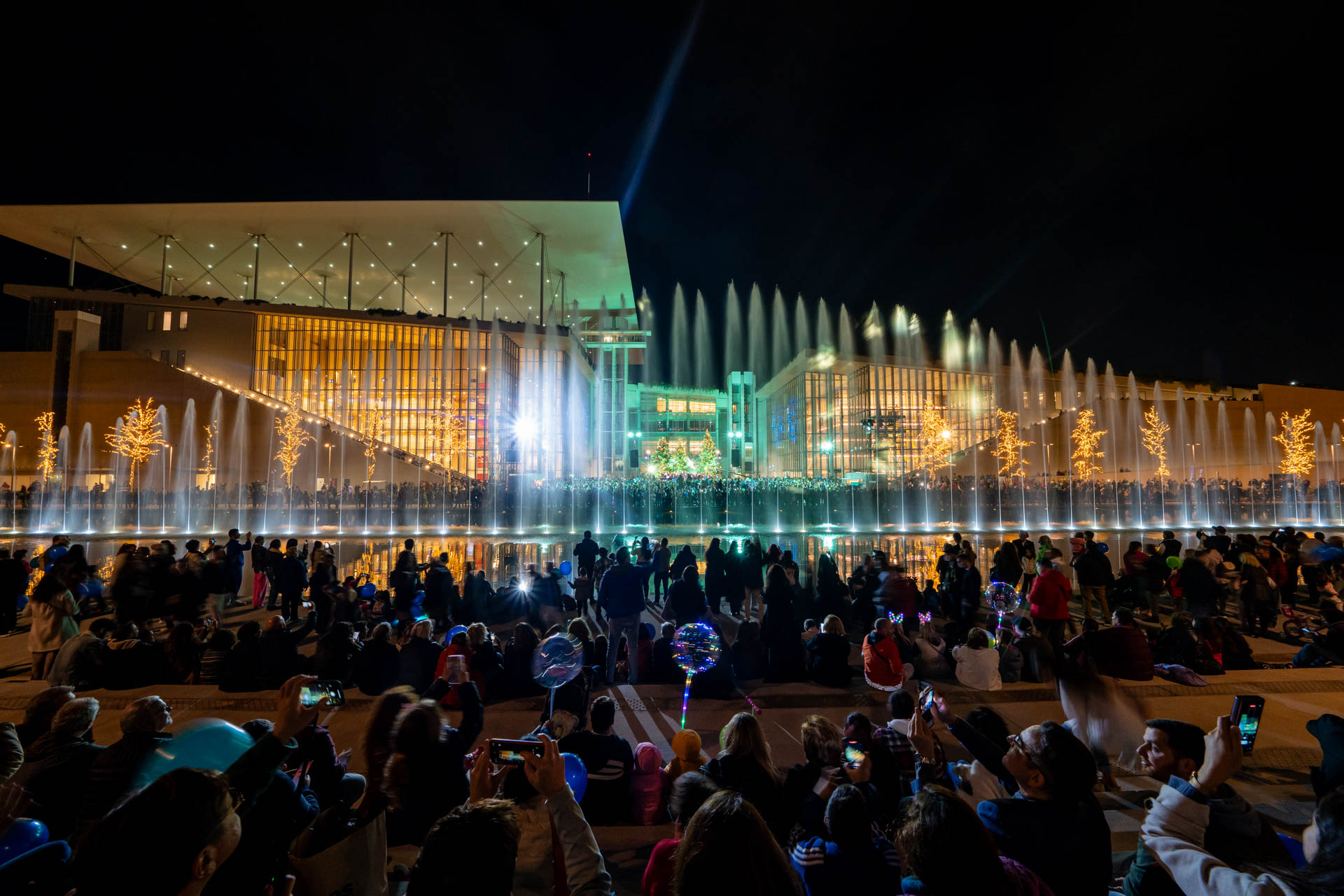 Πλήθος κόσμου παρακολουθεί το show των σιντριβανιών στο Κανάλι του Κέντρου Πολιτισμού Ίδρυμα Σταύρος Νιάρχος (ΚΠΙΣΝ) με φόντο τα χριστουγεννιάτικα δέντρα στο ΚΠΙΣΝ. 