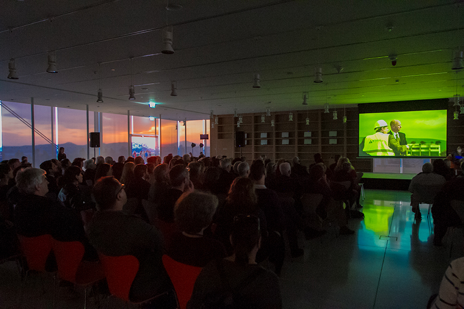 Μια φωτογραφία που δείχνει πλήθος κόσμου να κάθεται σε καρέκλες και να παρακολουθεί μια προβολή
