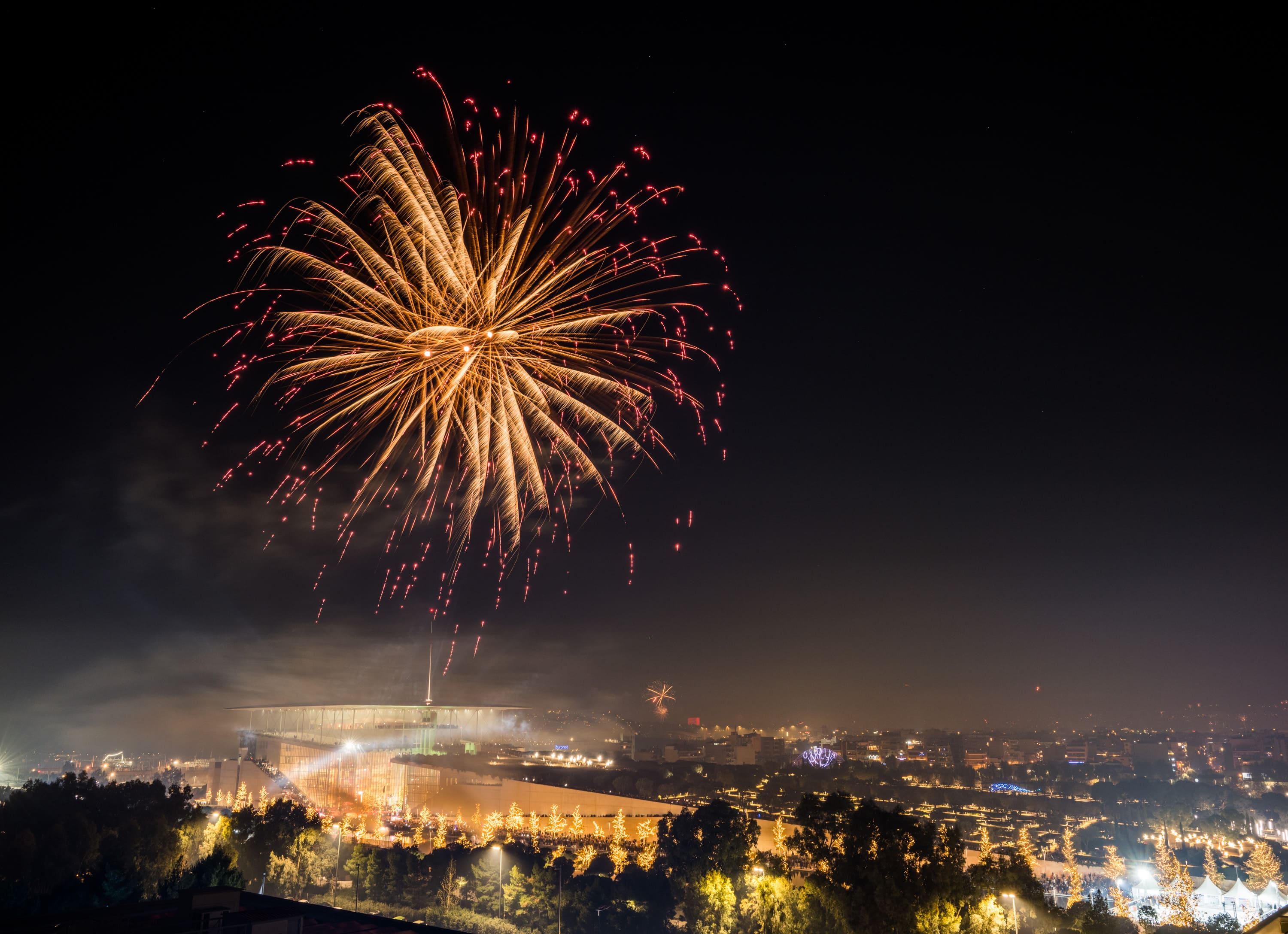 Αεροφωτογραφία του ΚΠΙΣΝ με κίτρινα και κόκκινα πυροτεχνήματα στον ουρανό.