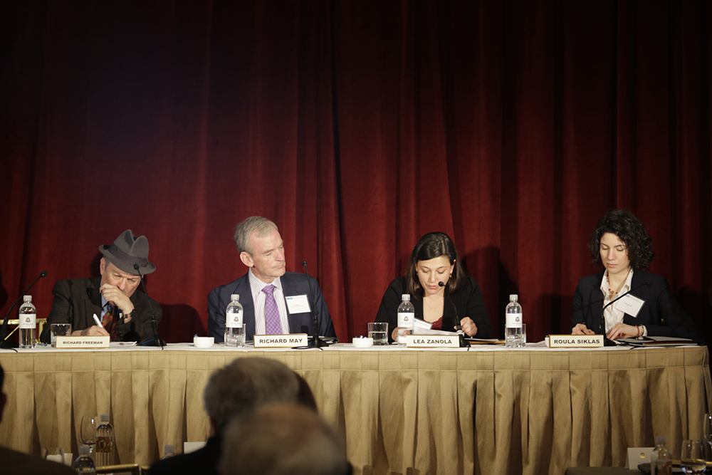 Τέσσερα άτομα κάθονται σε ένα τραπέζι συνεδριάσεων μπροστά σε κοινό