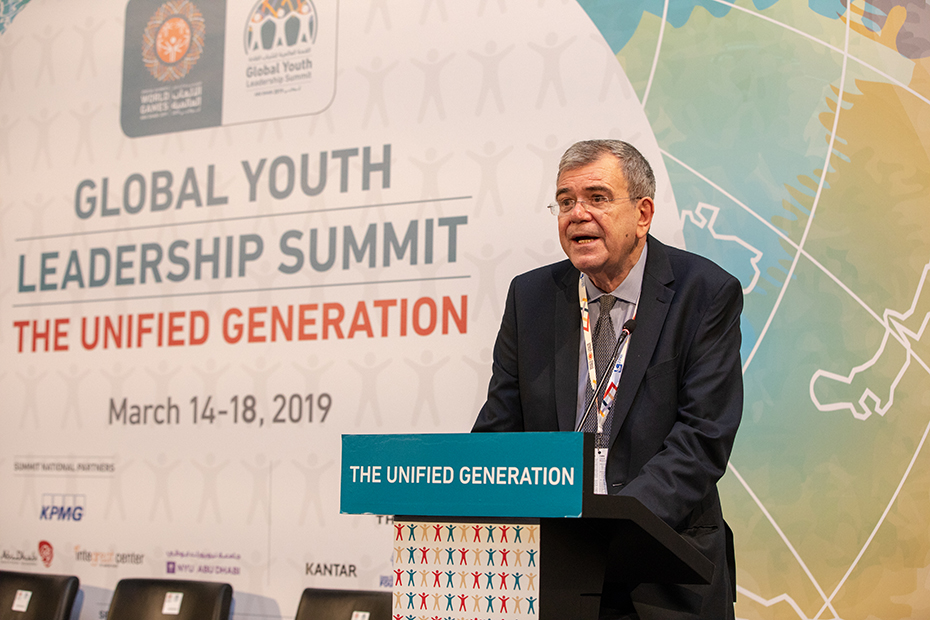 Ένας άνδρας μιλάει σε μια εξέδρα μπροστά από μια προβολή που γράφει 