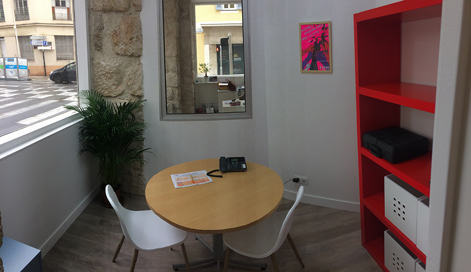 Ένα μικρό στρογγυλό τραπέζι με δύο καρέκλες και μια μικρή βιβλιοθήκη στον τοίχο δίπλα από ένα παράθυρο 