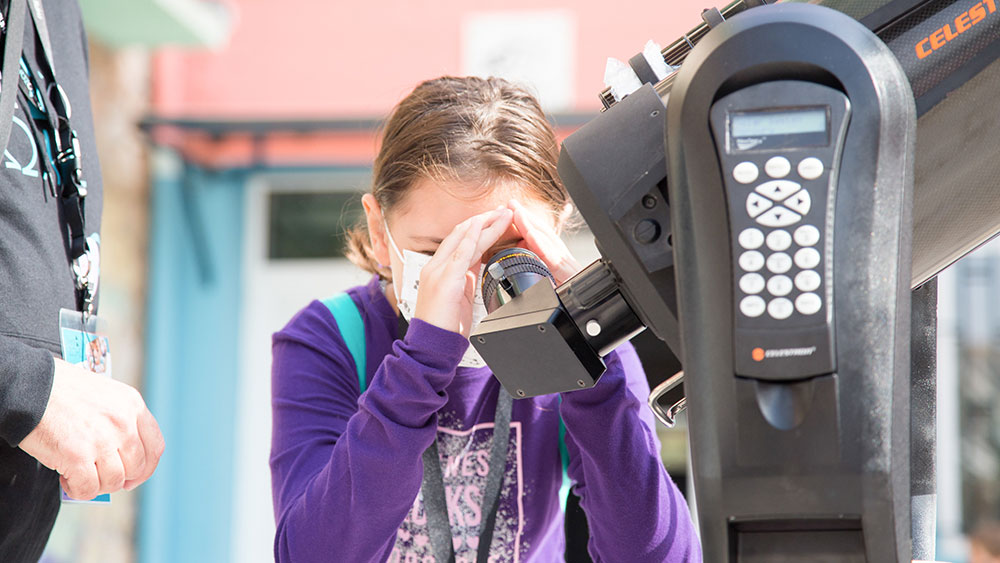 Ένα μικρό κορίτσι κοιτάει μέσα από ένα τηλεσκόπιο 