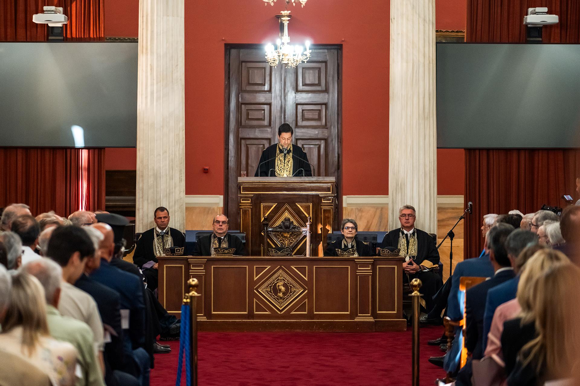 Ο Πρύτανης του ΕΚΠΑ, Καθηγητής Γεράσιμος Σιάσος, στέκεται όρθιος στο βήμα, ντυμένος με τήβεννο, καθώς εκφωνεί ομιλία.  