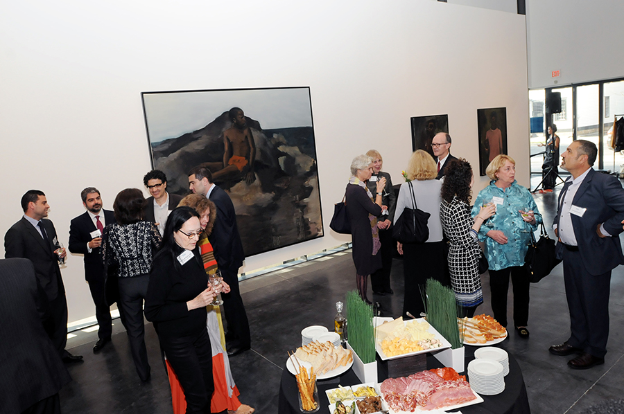 Φωτογραφία από έναν χώρο σε μια gallery στην οποία κόσμος έχει μοιραστεί σε ομάδες και συζητά και υπάρχει ένα τραπέζι με φαγητό 