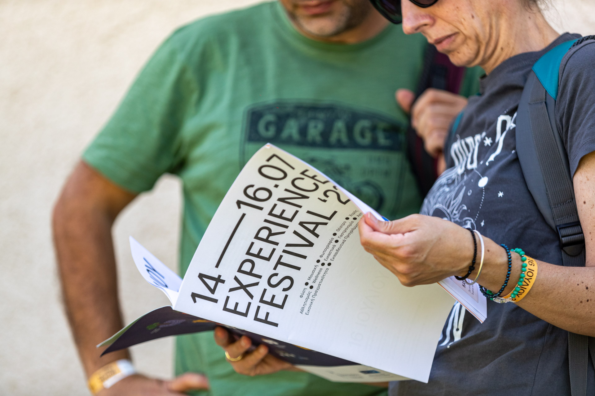 Δύο άτομα διαβάζουν το βιβλιαράκι Experience Festival 