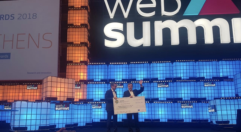 Μακρινή φωτογραφία στην οποία φαίνονται δυο άντρες στη σκηνή οι οποίοι κρατάνε μια επιταγή σε μέγεθος μακέτας και χαμογελούν 