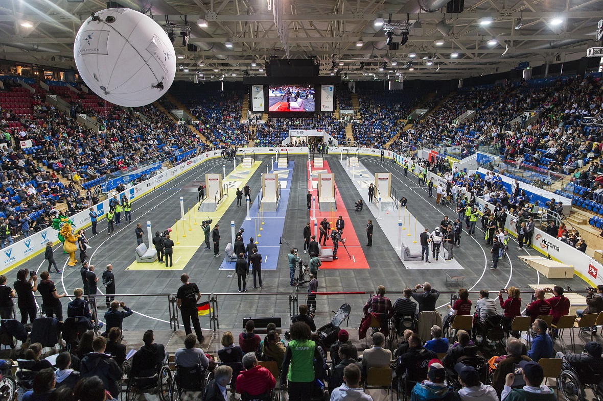 Μακρινή φωτογραφία από το εσωτερικό ενός σταδίου γεμάτο κόσμο στο οποίο υπάρχουν τέσσερις διαφορετικού χρώματος διάδρομοι ειδικά διαμορφωμένοι για τους συμμετέχοντες με κινητές δυσκολίες στα πλαίσια του Rehab Initiative