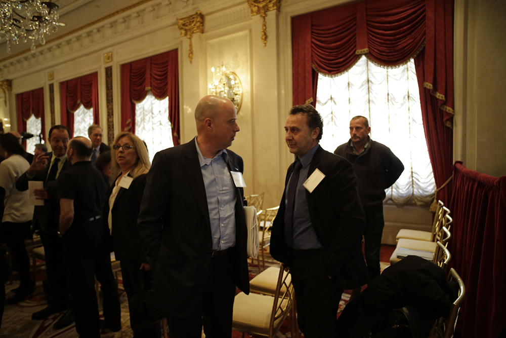 Ο Ανδρέας Δρακόπουλος και ένας άνδρας μιλούν σε ένα δωμάτιο γεμάτο κόσμο