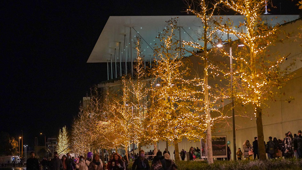 Κόσμος συγκεντρωμένος στο Κέντρο Πολιτισμού Ίδρυμα Σταύρος Νιάρχος, όπου τα δέντρα είναι στολισμένα με φώτα 