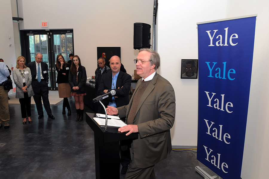 Ένας άντρας μιλάει στο βήμα ενώ πίσω του υπάρχει ένα banner το οποίο γράφει Yale και κόσμος στέκεται όρθιος και τον ακούει