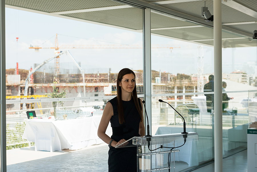 Μια γυναίκα δίνει ομιλία, ενώ στο παρασκήνιο διακρίνεται η οικοδομή